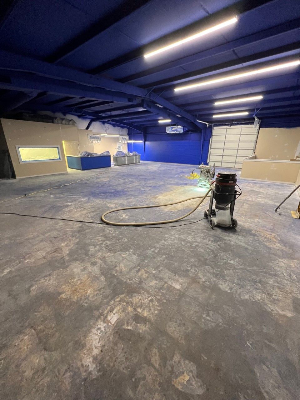 Dirty commercial kitchen under construction. Concrete floor, exposed walls, and a counter with covered items.