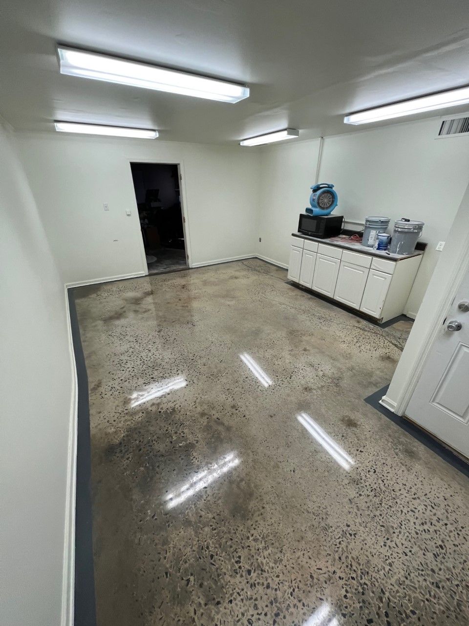 Polished concrete floor in a brightly lit room with white walls, a cabinet, and a doorway.