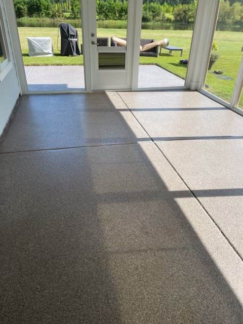 A sunroom with a speckled, shiny floor, glass windows, and a door leading to an outdoor patio and green yard.