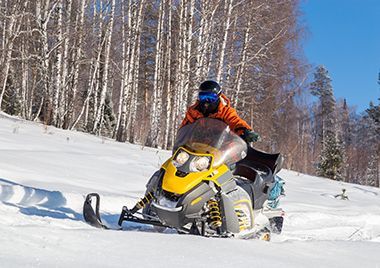 A man is riding a snowmobile down a snow covered hill.