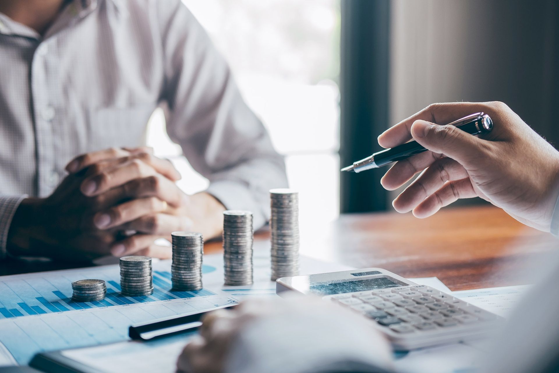 Hands reviewing financial charts with stacked coins and a calculator on a desk