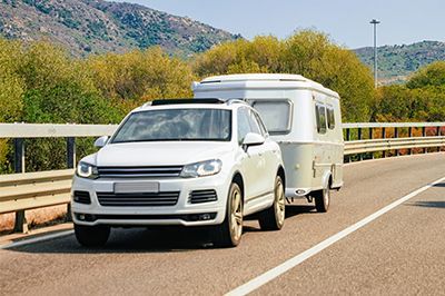 A white suv is towing a trailer down a highway.