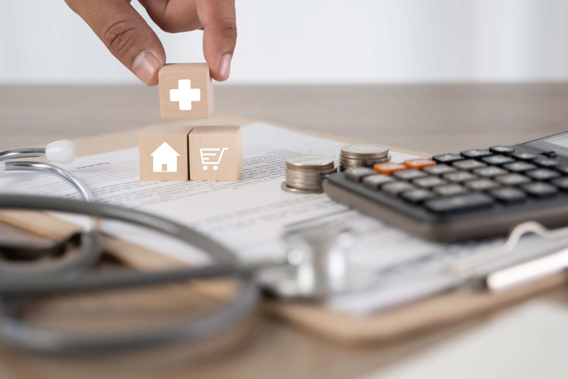 Hand placing a wooden house icon on financial charts beside a calculator and coins