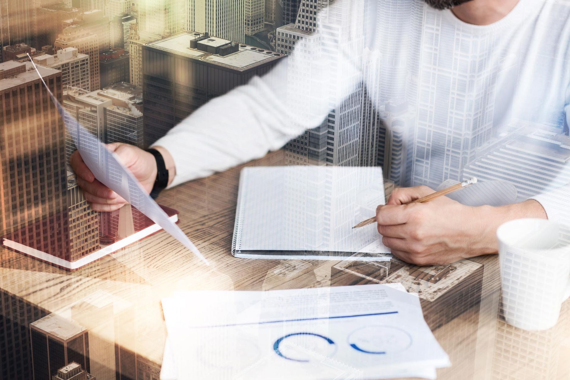 Person working at a desk with laptop, notebook, charts, and a coffee cup overlaid with a city skyline.