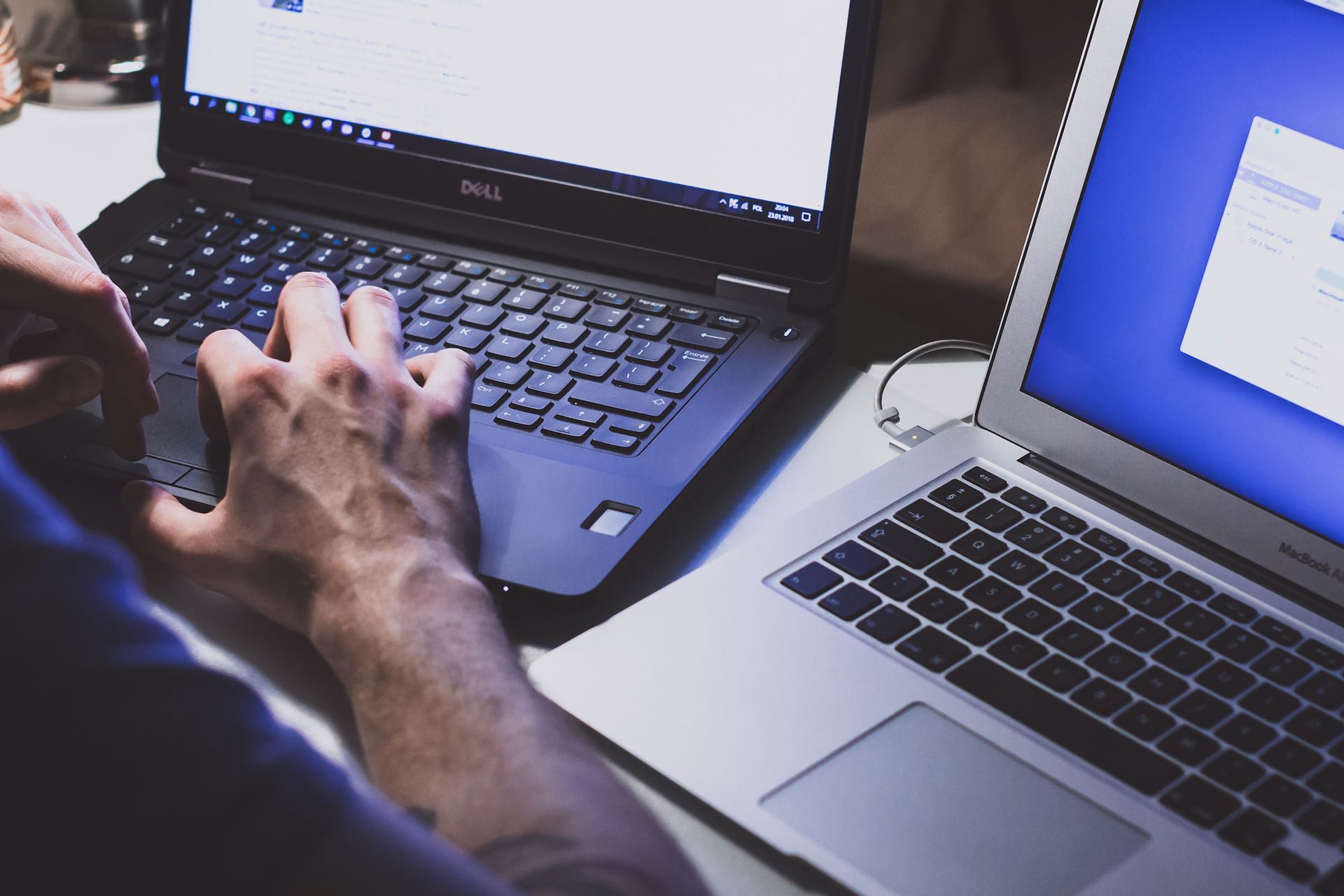 Person typing on a laptop beside another open laptop on a desk.