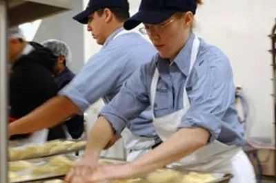 Workers in blue uniforms and caps preparing food on a production line