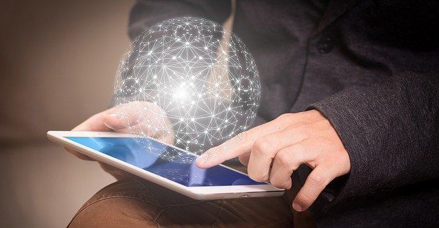 Hands using a tablet with a glowing digital network orb above it