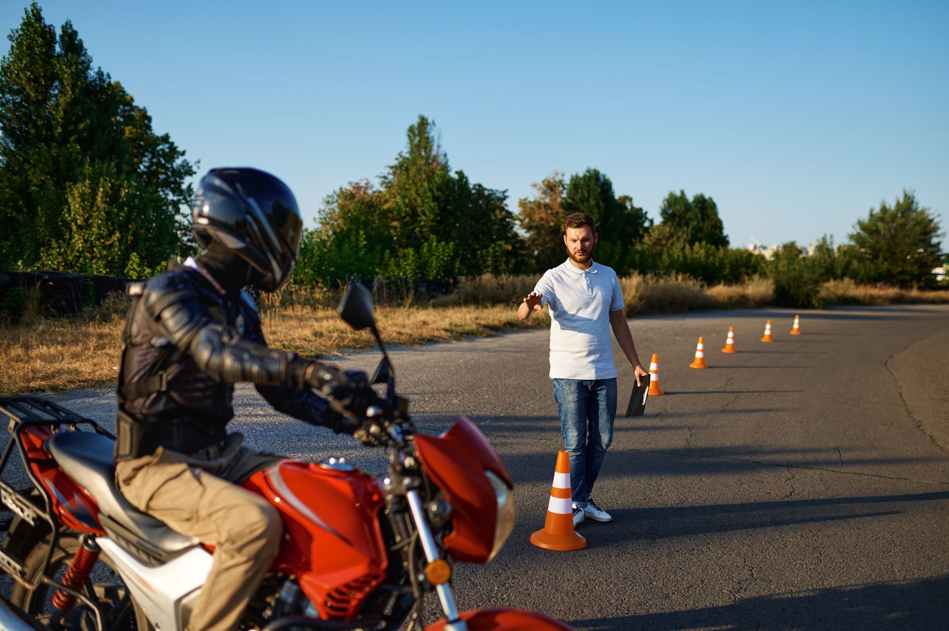 A man is riding a motorcycle next to a man standing next to a traffic cone