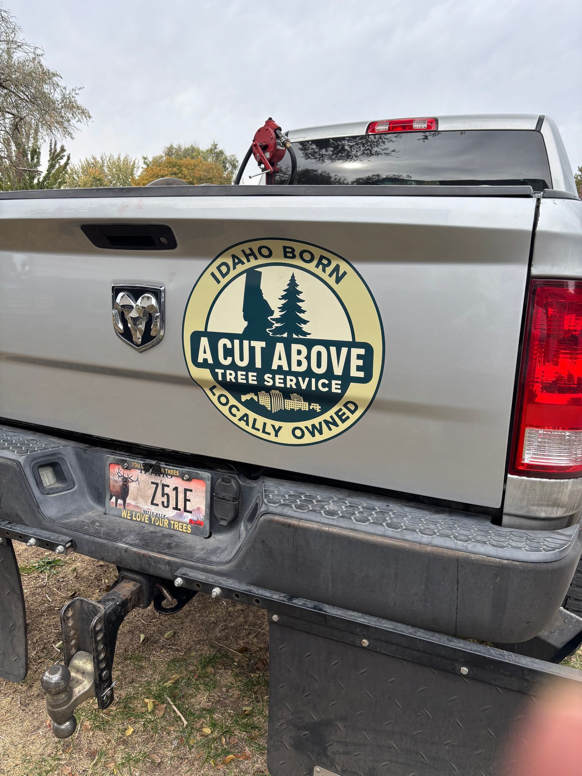 White pickup truck tailgate with a circular “A Cut Above Tree Service” logo and hitch on a gravel drive