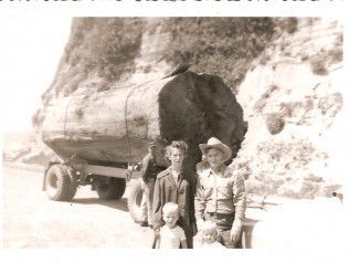 Three people posing beside a large truck loaded with a huge rock on a canyon road