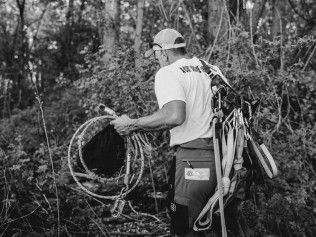 Worker carrying coiled cables and tools through a wooded area