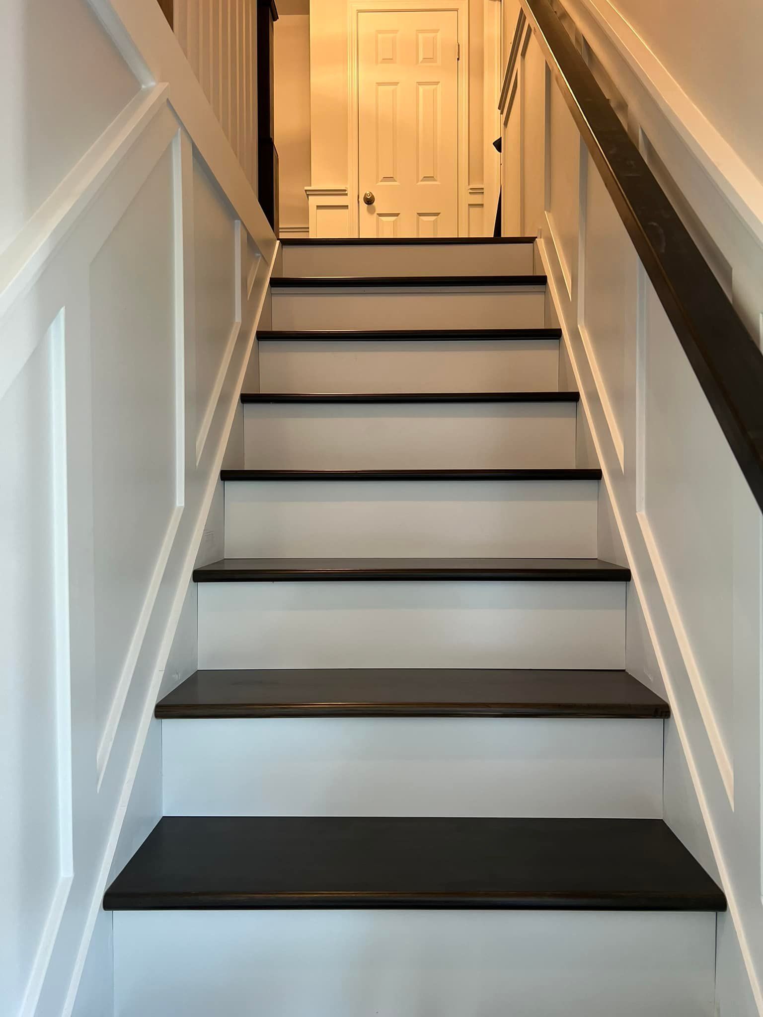 A set of stairs with black steps and a white railing leading up to a door.