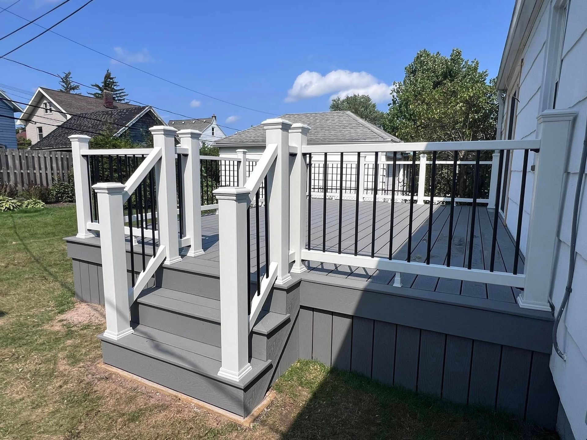 A deck with stairs and a white railing is in front of a house.