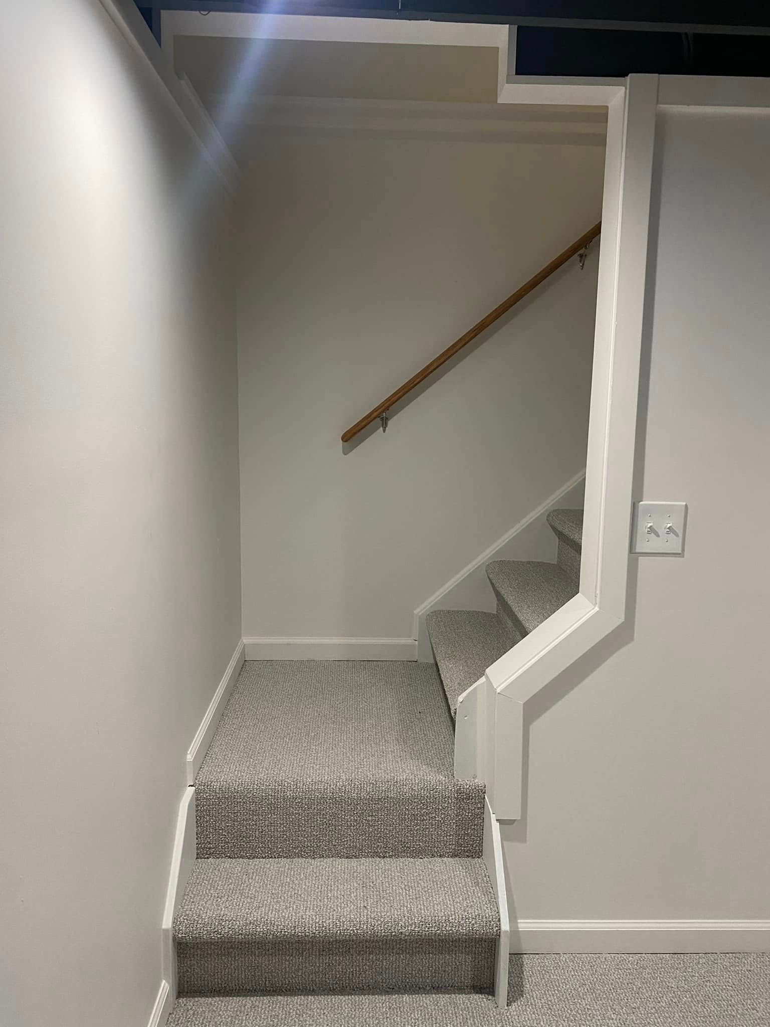 A staircase in a basement with carpeted steps and a wooden railing.