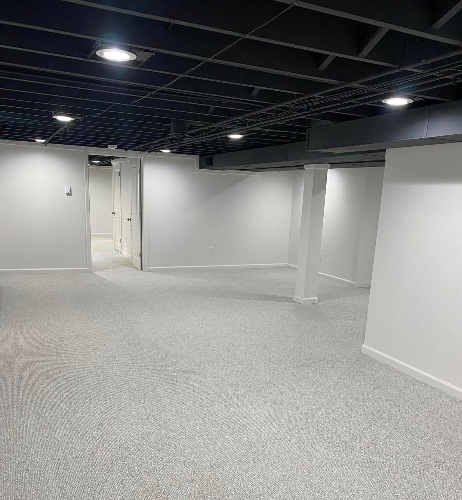 An empty basement with white walls and a black ceiling.
