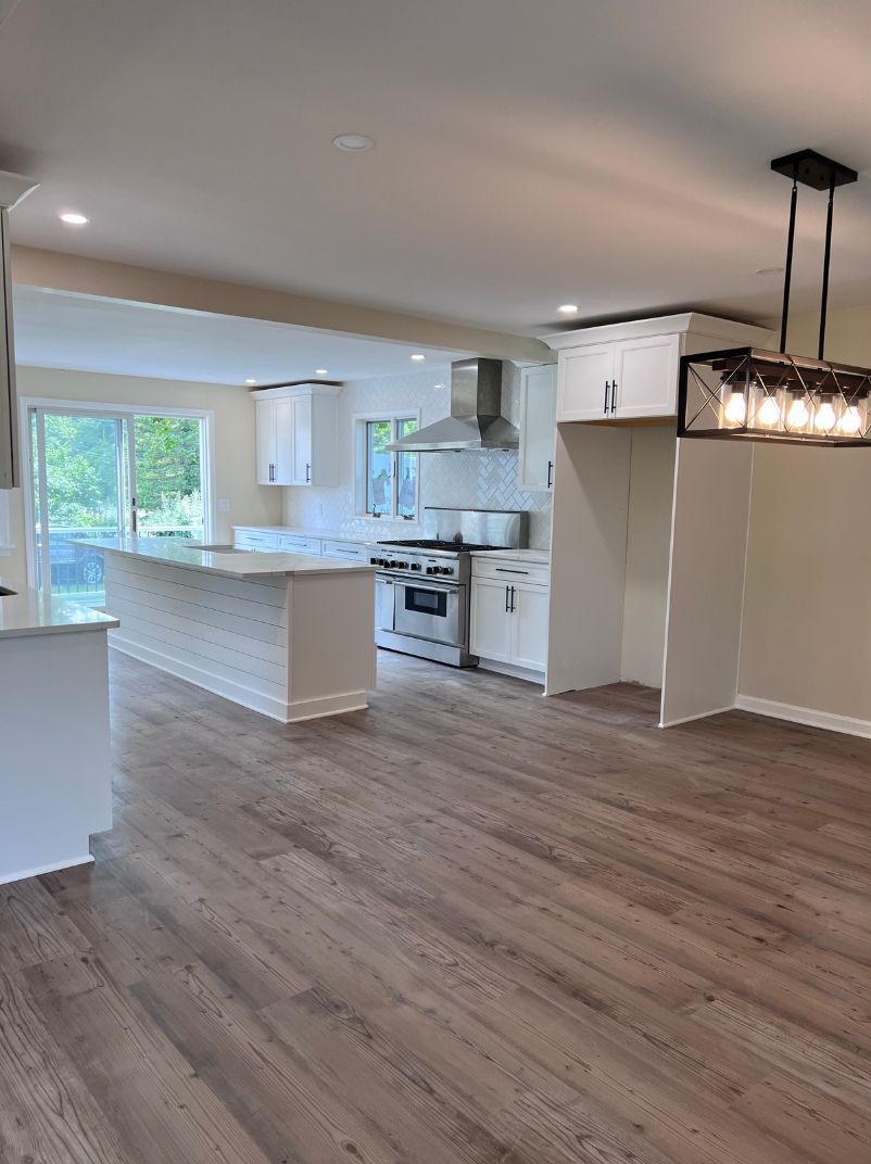 An empty kitchen with hardwood floors and white cabinets.