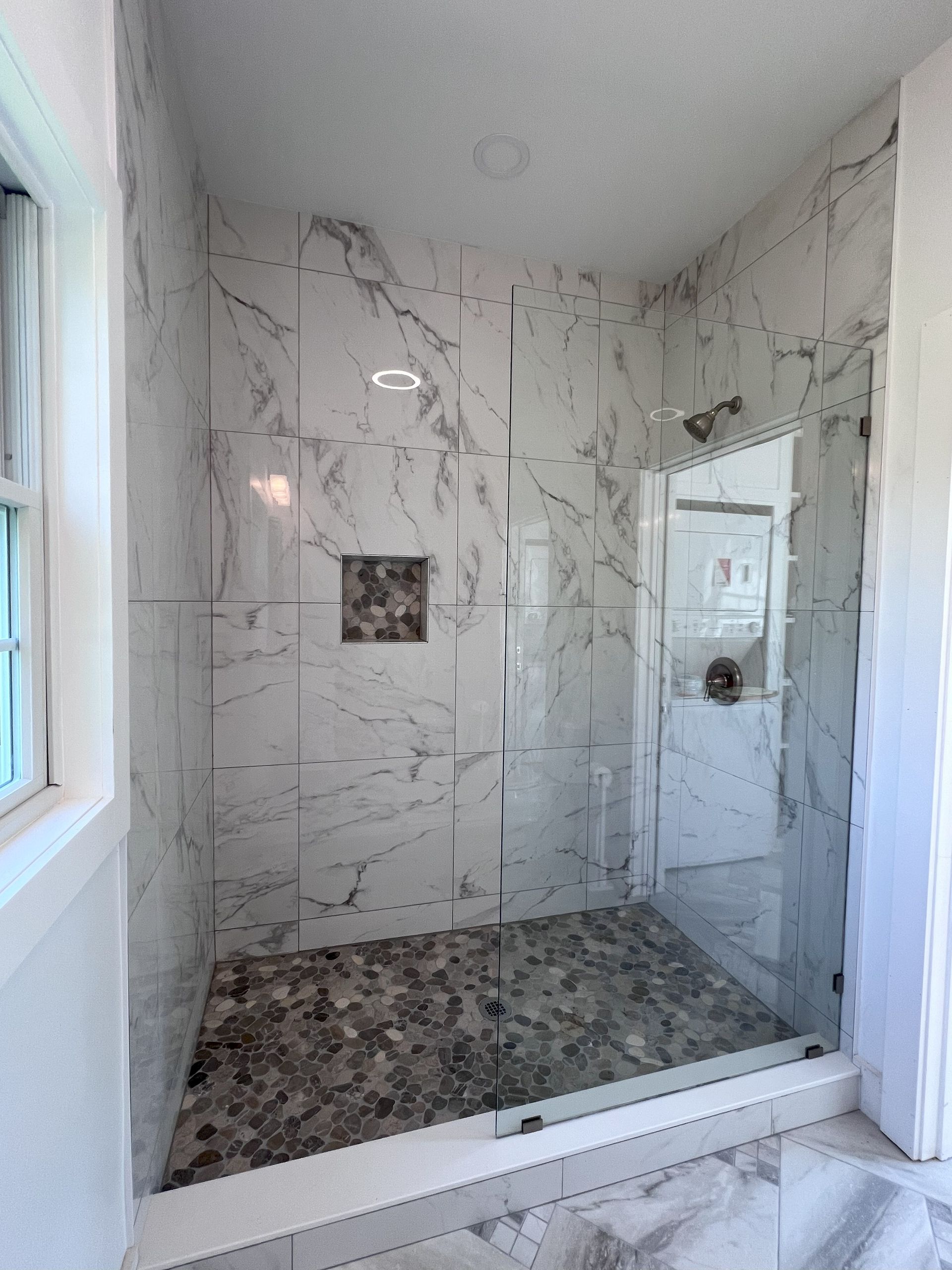 A bathroom with marble tiles and a walk in shower with a glass door.