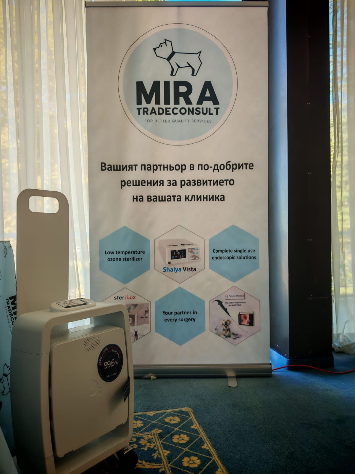 Банер за Mira Tradeconsult: лого на куче, текст, шест икони. Пречиствател на въздух е разположен пред банера.