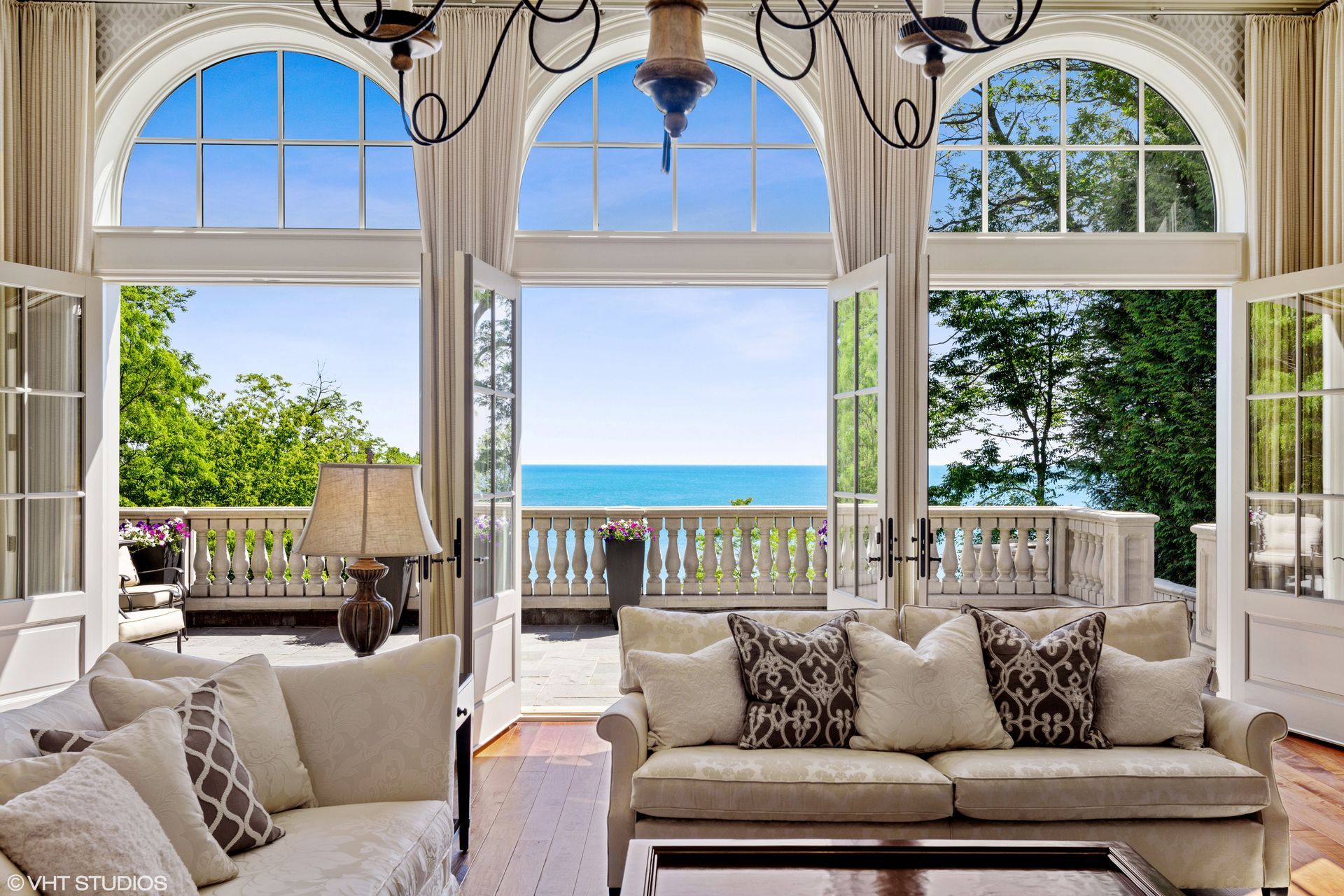 A view through double doors into a dining room with a round white table, dark chairs, and a globe chandelier.
