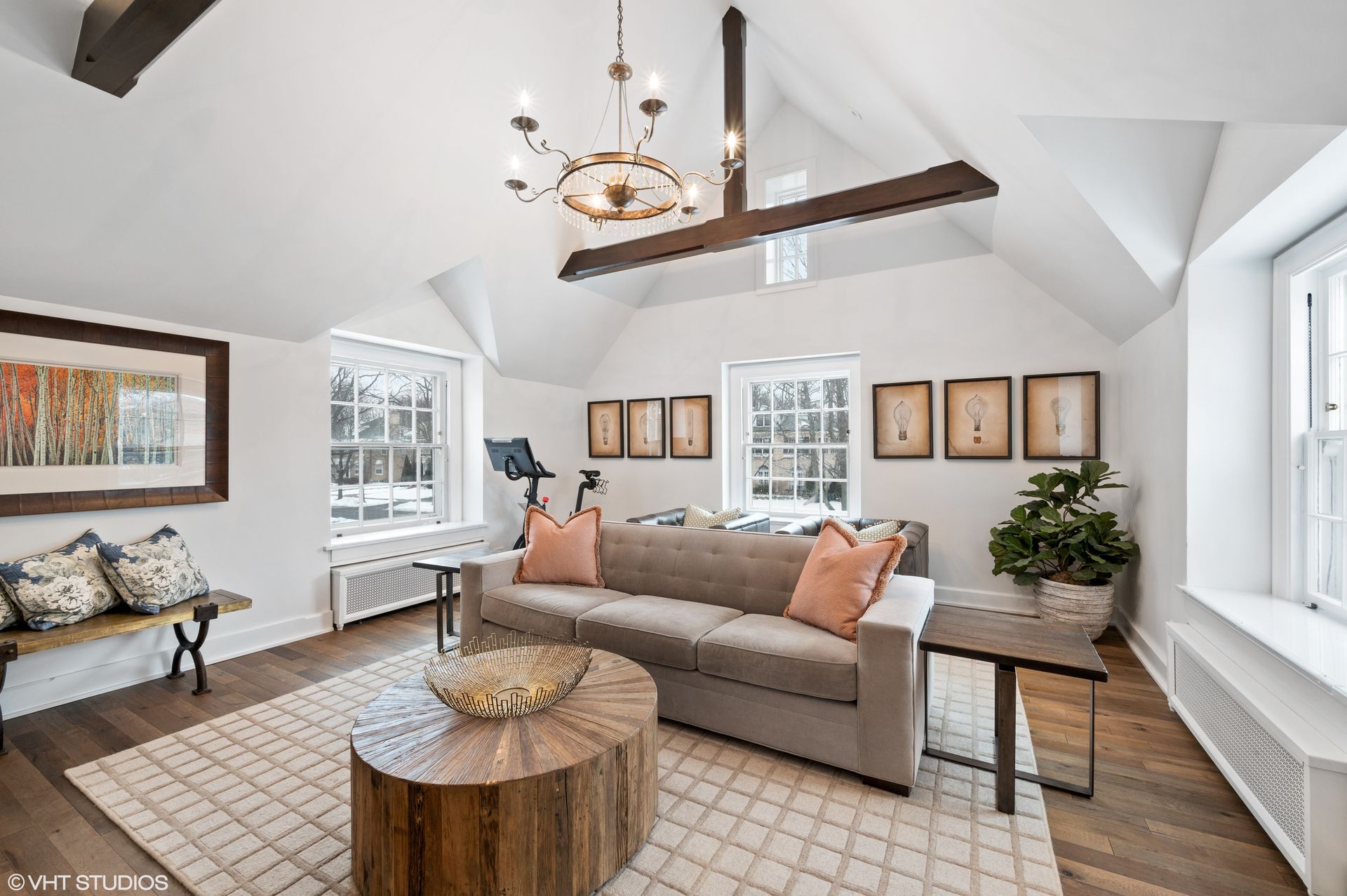 A bright living room with a fireplace, television, built-in shelves, a round olive ottoman, and patterned furniture.