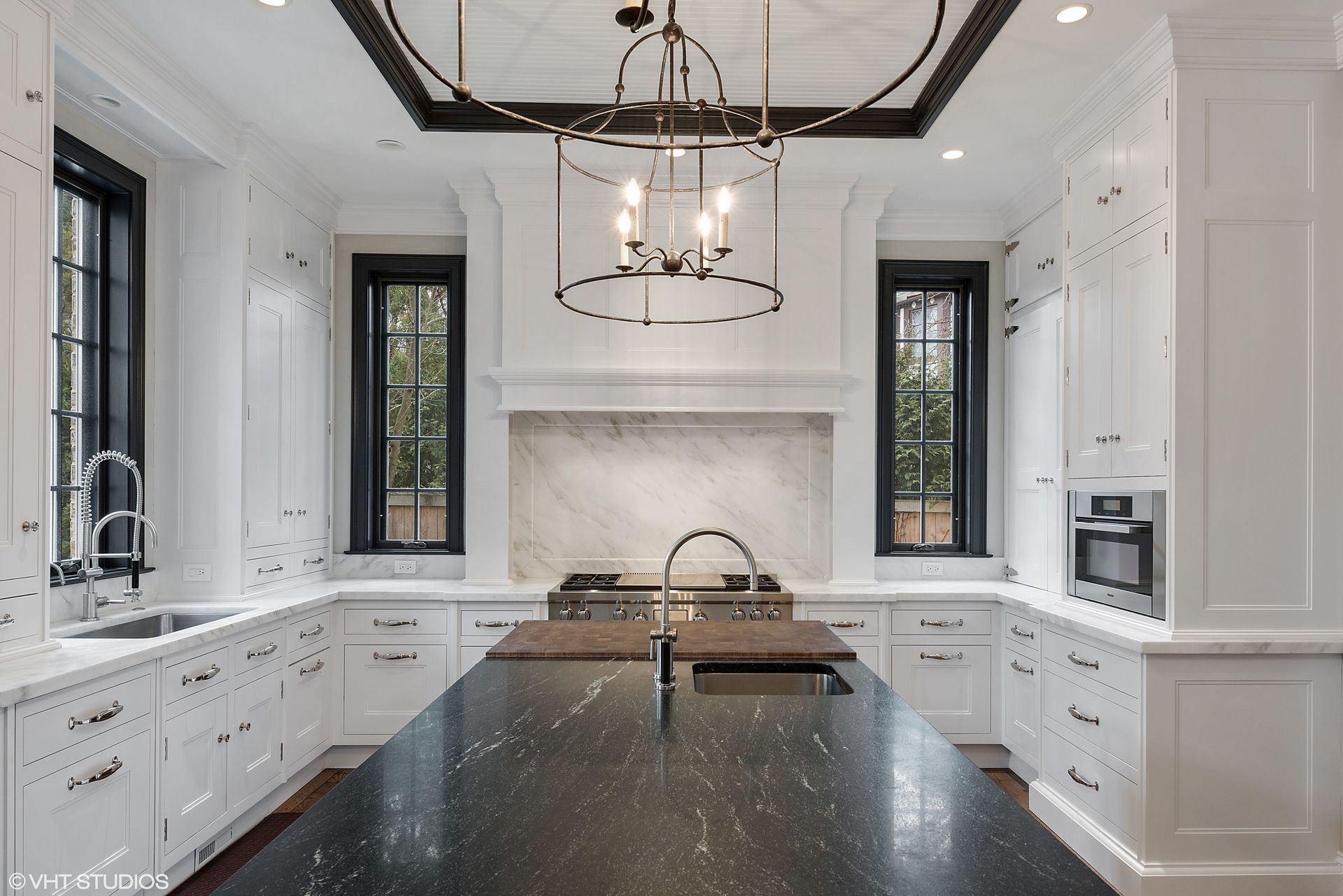 Bright modern kitchen with white cabinets, black countertops, central island, and pendant lights