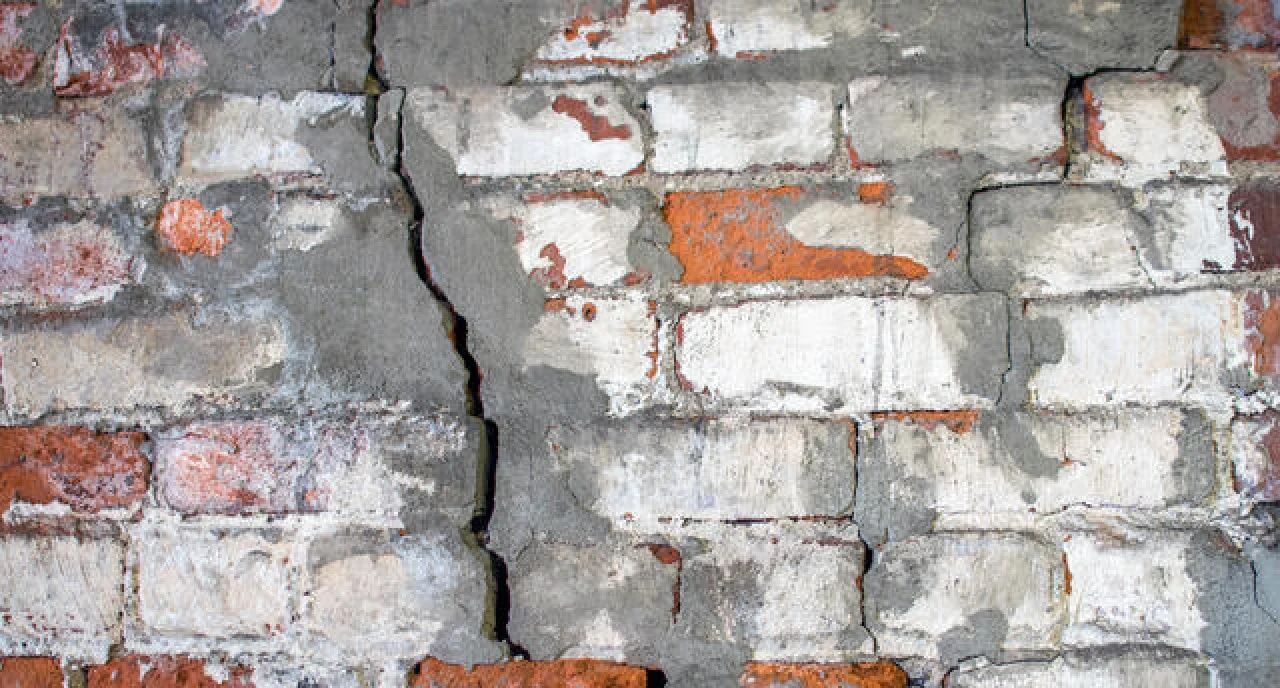 Cracked white brick wall with patches of exposed red brick and peeling gray paint