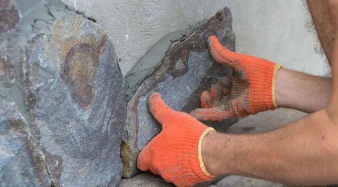 Hands in orange gloves fitting a dark stone into a wall gap