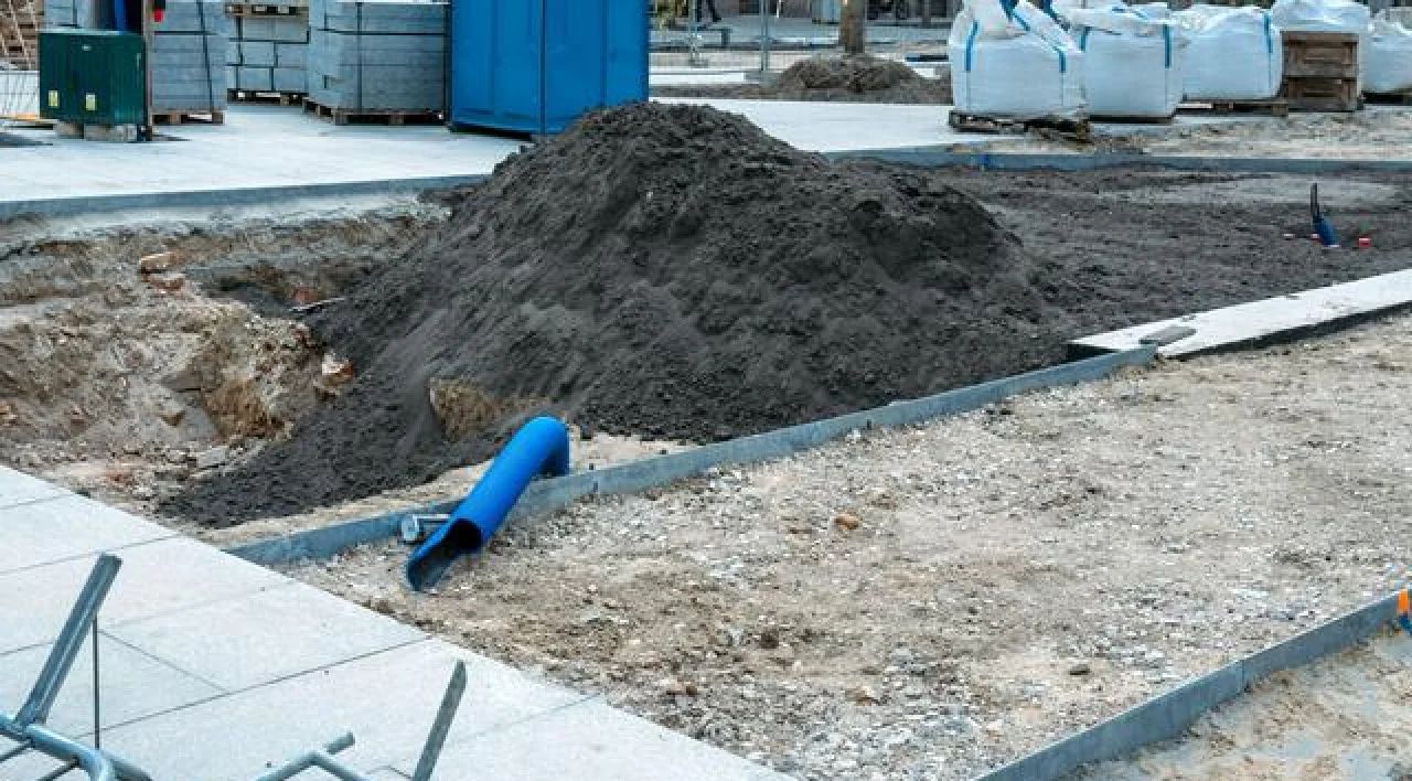 Construction site with large dirt pile, blue pipe, and concrete curbing around a dug-out area