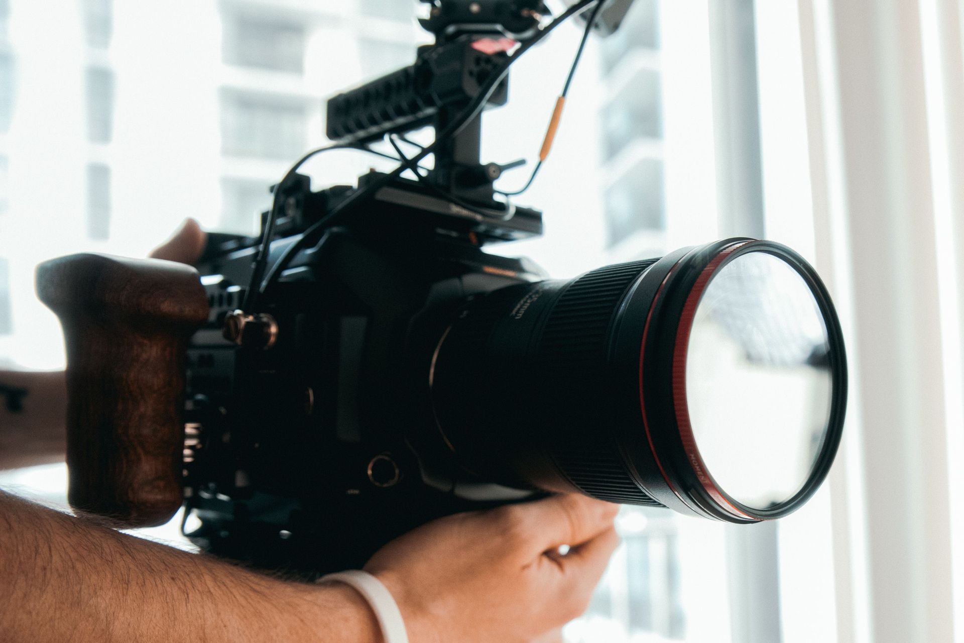 Professionele videocamera met grote lens, binnenshuis bij een raam geplaatst.