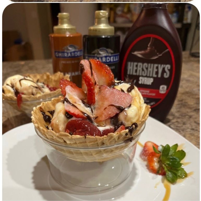 Ice cream sundae in a waffle bowl with strawberries and syrup.