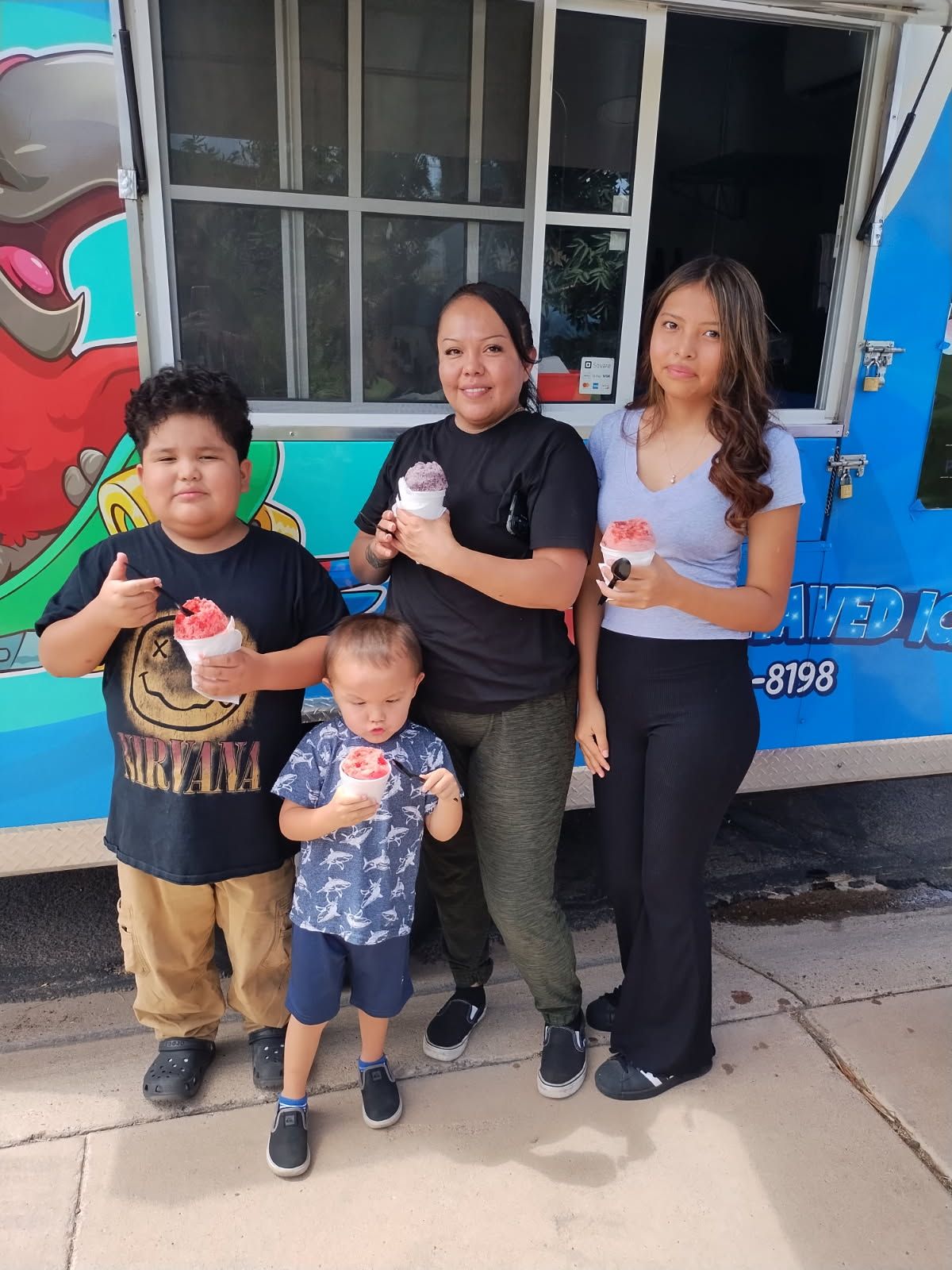 Family of four with shaved ice treats in front of a food truck; smiling.