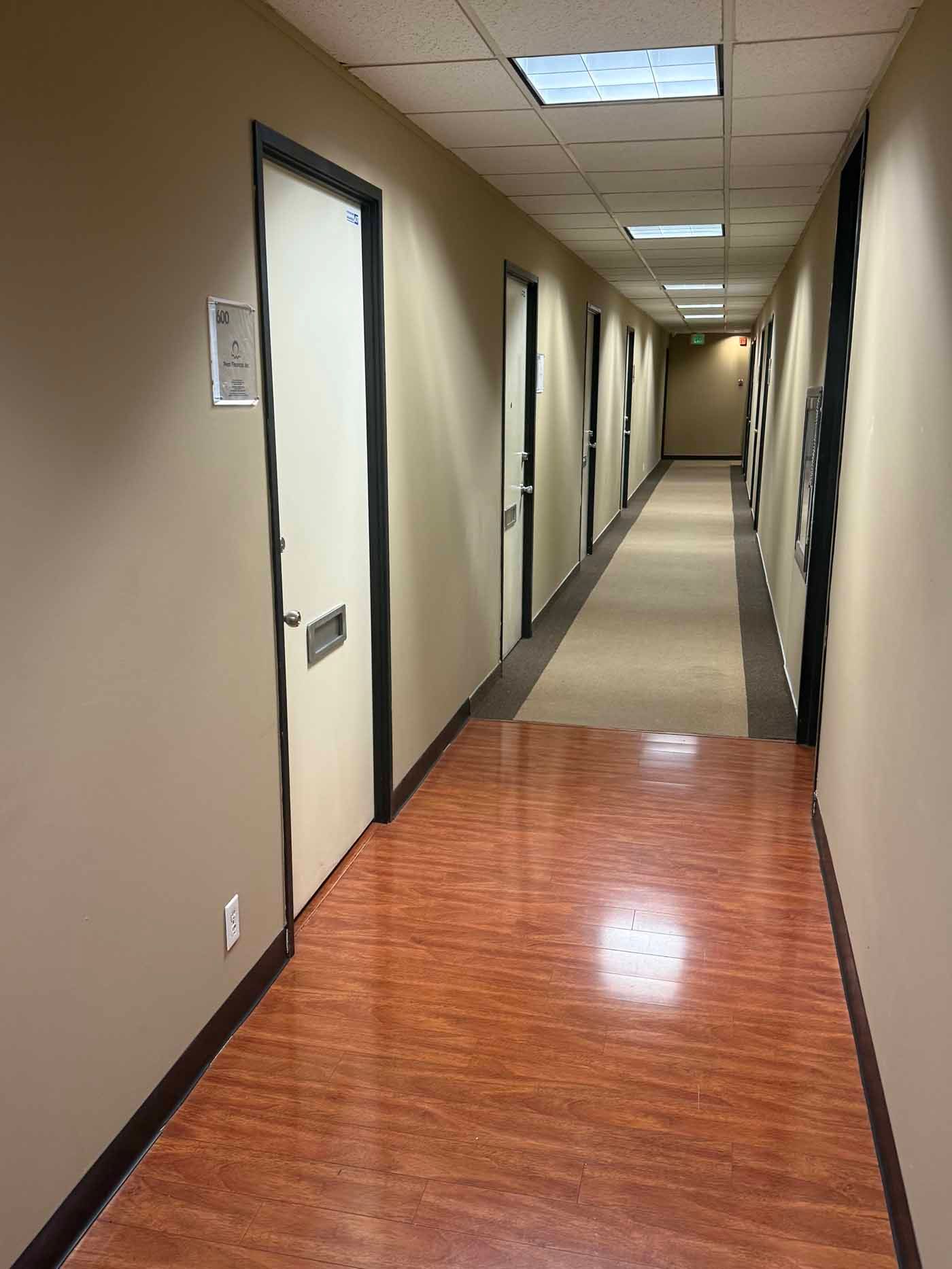 Office hallway with beige walls, wood floor, closed doors, and fluorescent ceiling lights