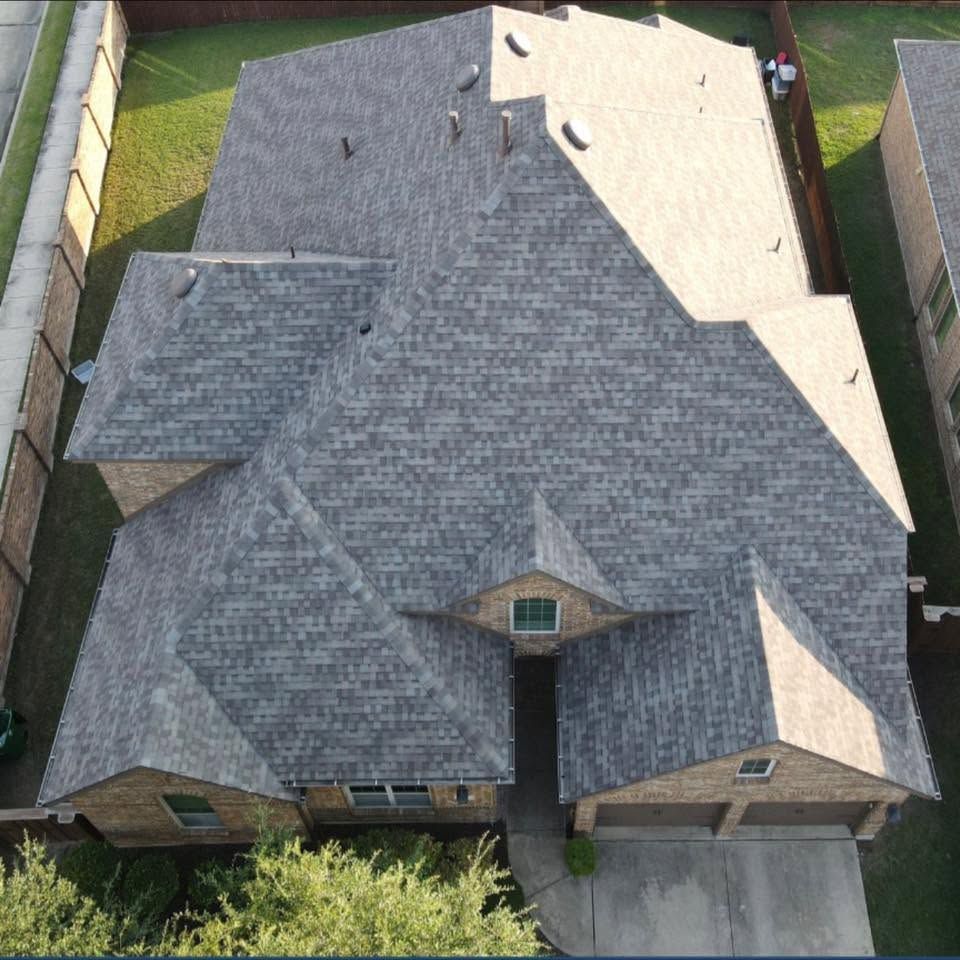 Aerial view of a house with a dark gray roof, front driveway, and fenced backyard.