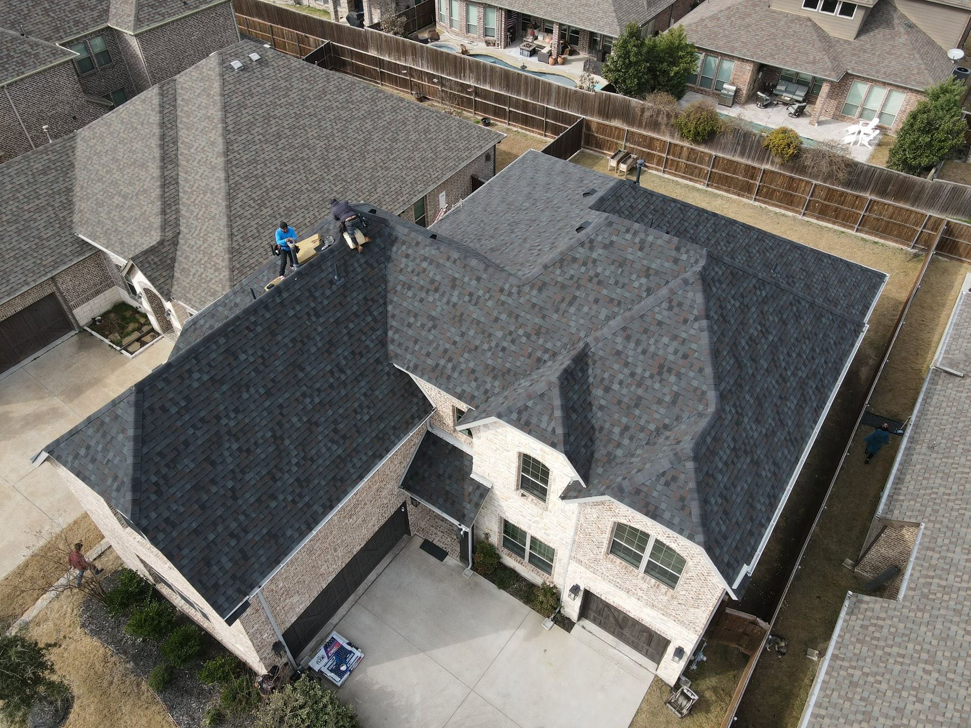 Aerial view of a large gray-roofed suburban house with a driveway and fenced backyard.