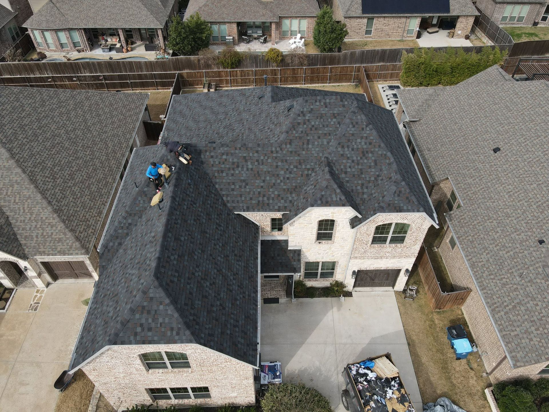Aerial view of a white house with a dark roof and backyard, surrounded by neighboring homes and driveways.