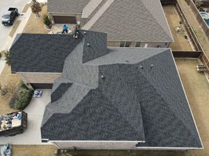 Aerial view of a suburban house with dark gray roofs and a driveway beside neighboring homes.