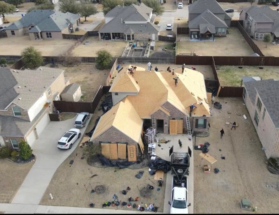 Aerial view of a house with severe roof damage, debris, and vehicles in a suburban neighborhood.
