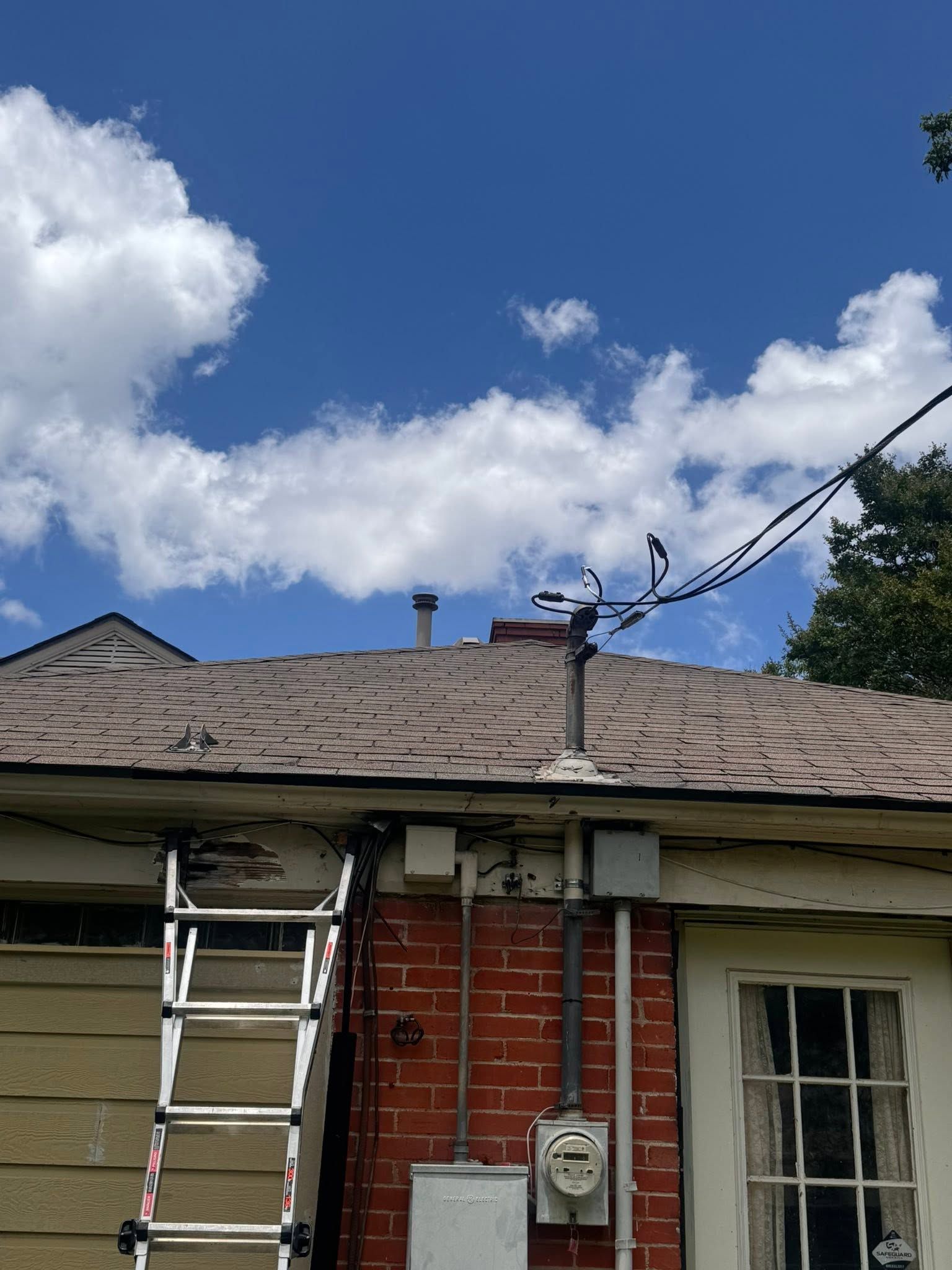 Back of a house with a ladder against the roof under a blue sky with clouds