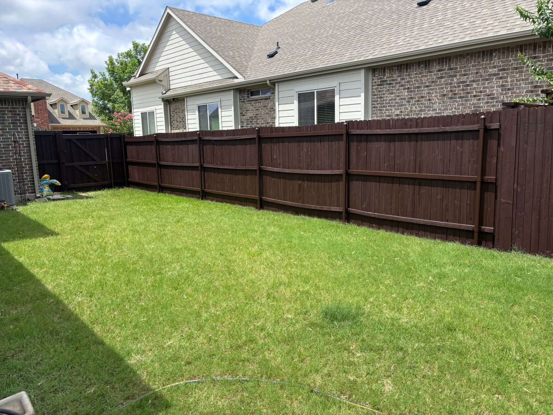Backyard with green lawn, brown wooden fence, and brick house with white trim.