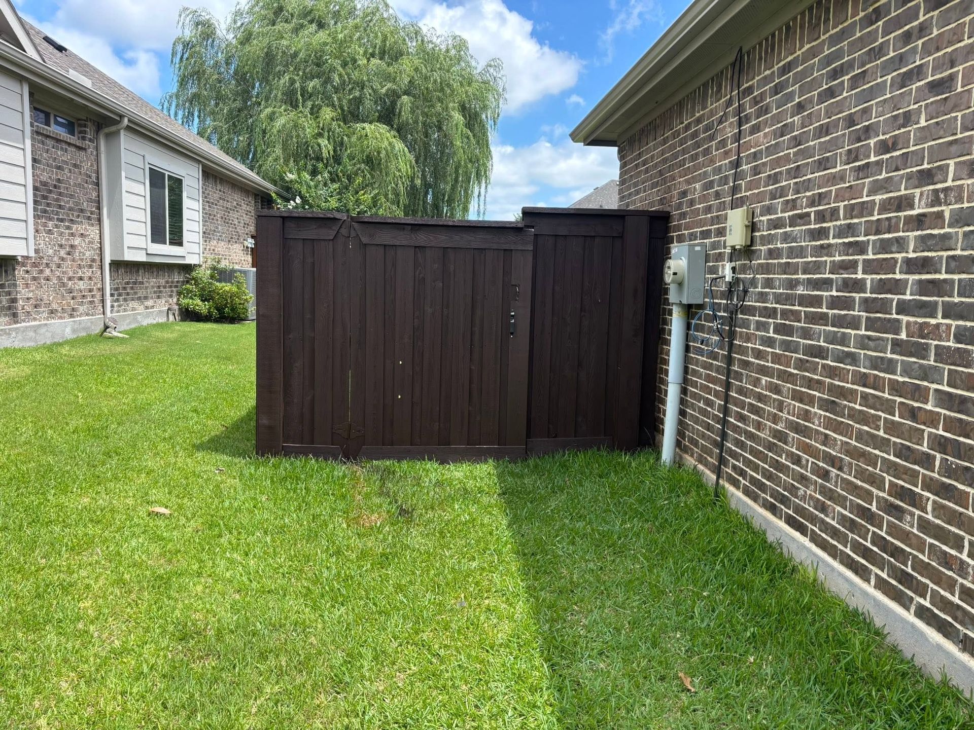 Backyard view of a dark brown wooden fence beside a brick house and green lawn