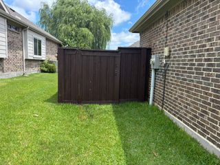 Backyard view of a dark brown wooden fence beside a brick house and green lawn