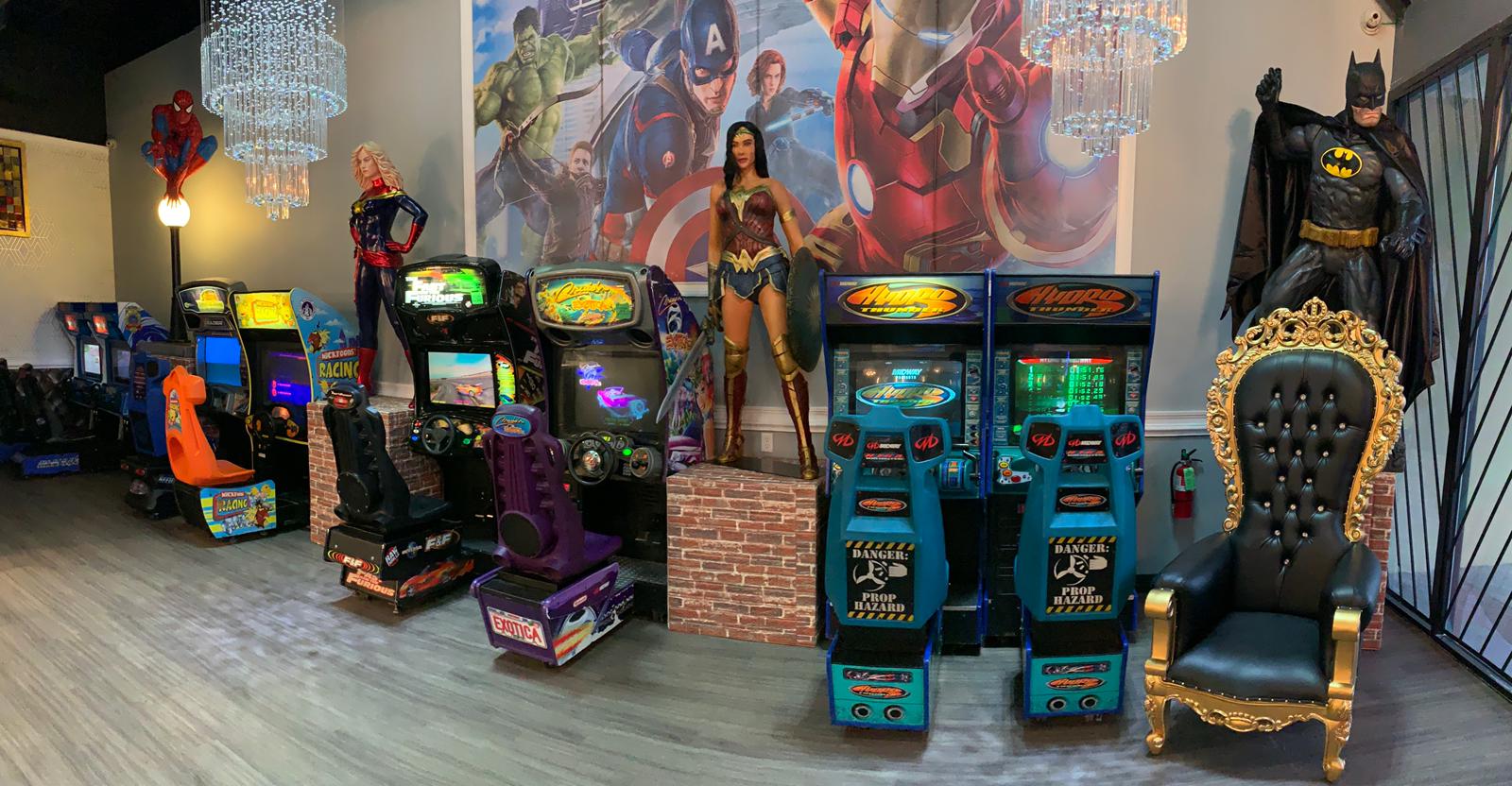 Row of colorful arcade machines and themed game cabinets, including Batman, in an indoor game room