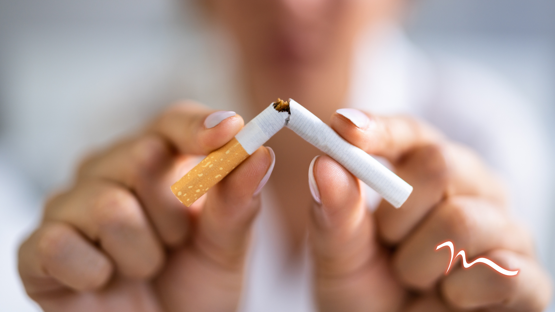 Person breaking a lit cigarette in half against a blurred background