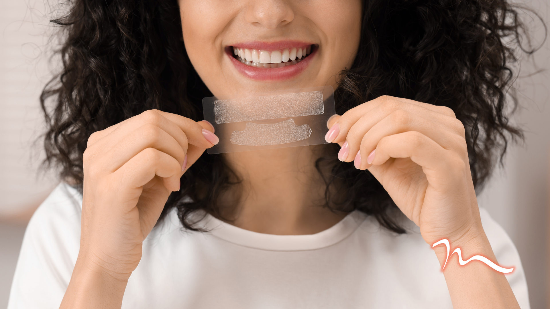 Woman smiling while holding a clear dental aligner in front of her mouth