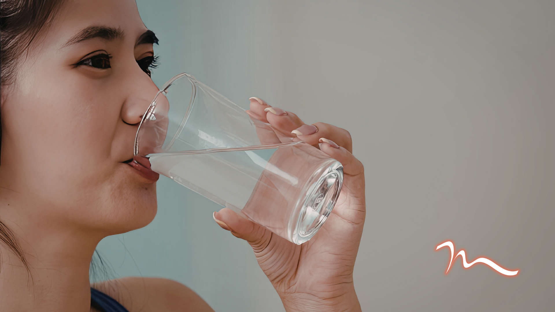 Close-up of a woman drinking water from a clear glass against a soft pink background