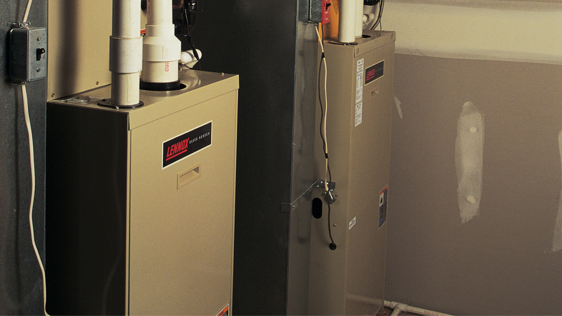 Two beige water heaters with pipes in a utility room