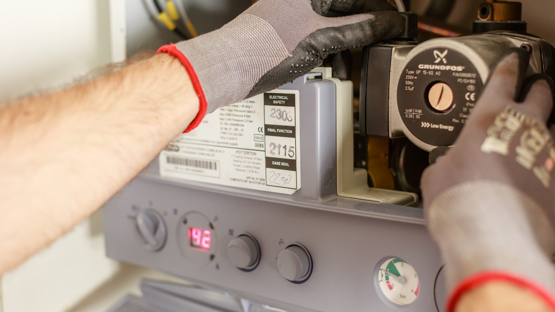 Gloved hands adjusting a furnace control panel with a lit red digital display
