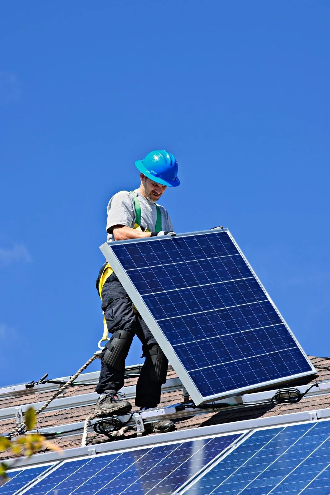 Worker installing a solar panel on a rooftop under a clear blue sky