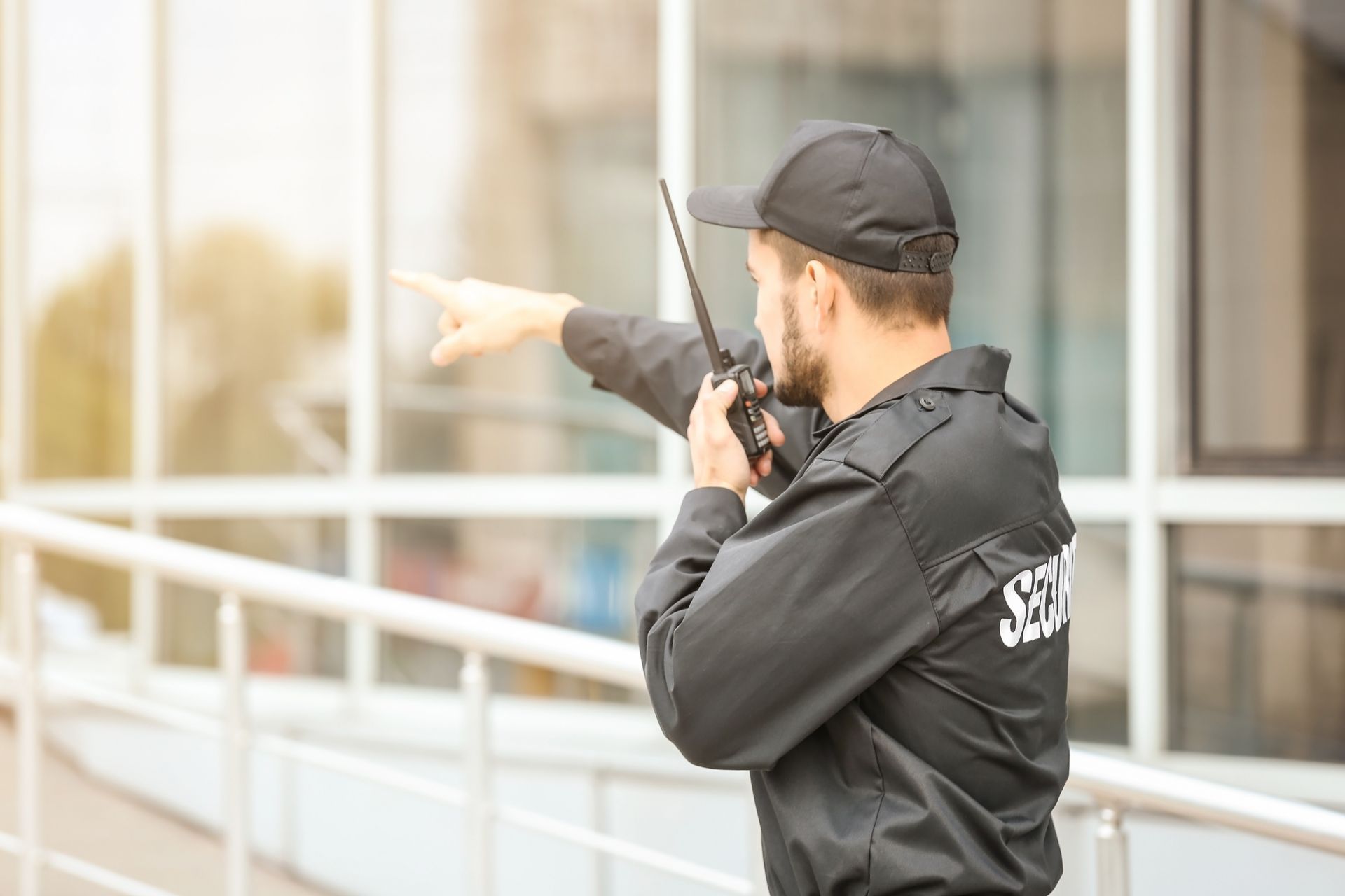 Security guard in black uniform pointing while speaking into a radio outside a building