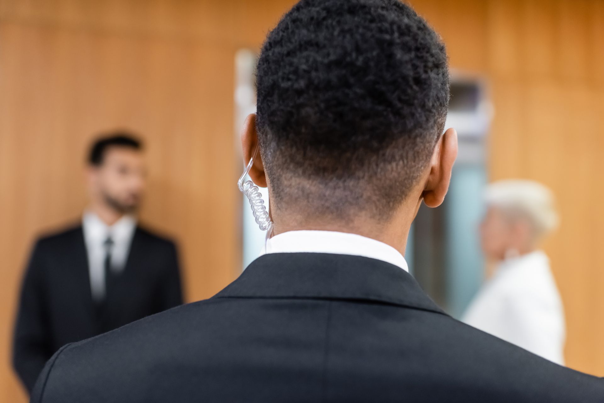 Person in a black suit faces a wedding ceremony with bride and officiant blurred in the background